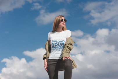 Camping T-Shirt Mockup Featuring a Stylish Woman Posing Against a Blue Sky 