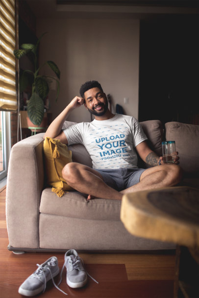 T-Shirt Mockup of a Man Sitting on a Couch Smiling at the Camera