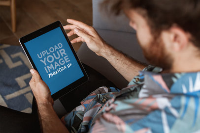 Overshoulder iPad Mockup of a Man Wearing a Shirt on his Sofa 22603