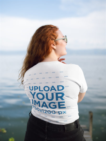 Back View T-Shirt Mockup of a Red-Haired Woman Facing a Lake