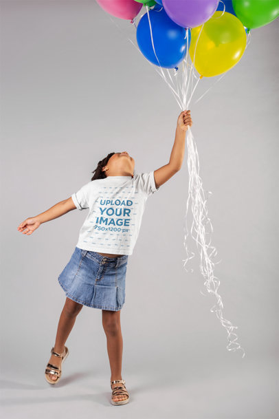 Mockup of a Little Girl Wearing a T-Shirt Holding Balloons in a Studio