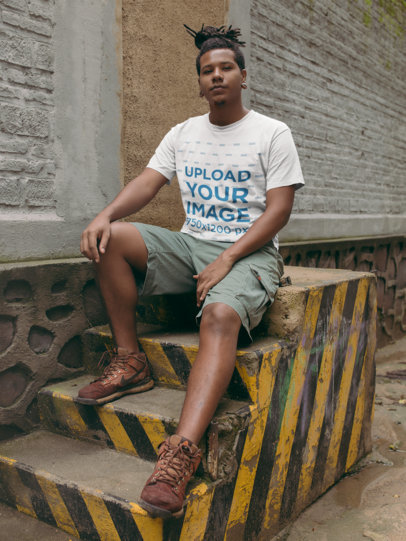 T-Shirt Mockup of a Man with Locks Sitting Next to a Sealed Entrance