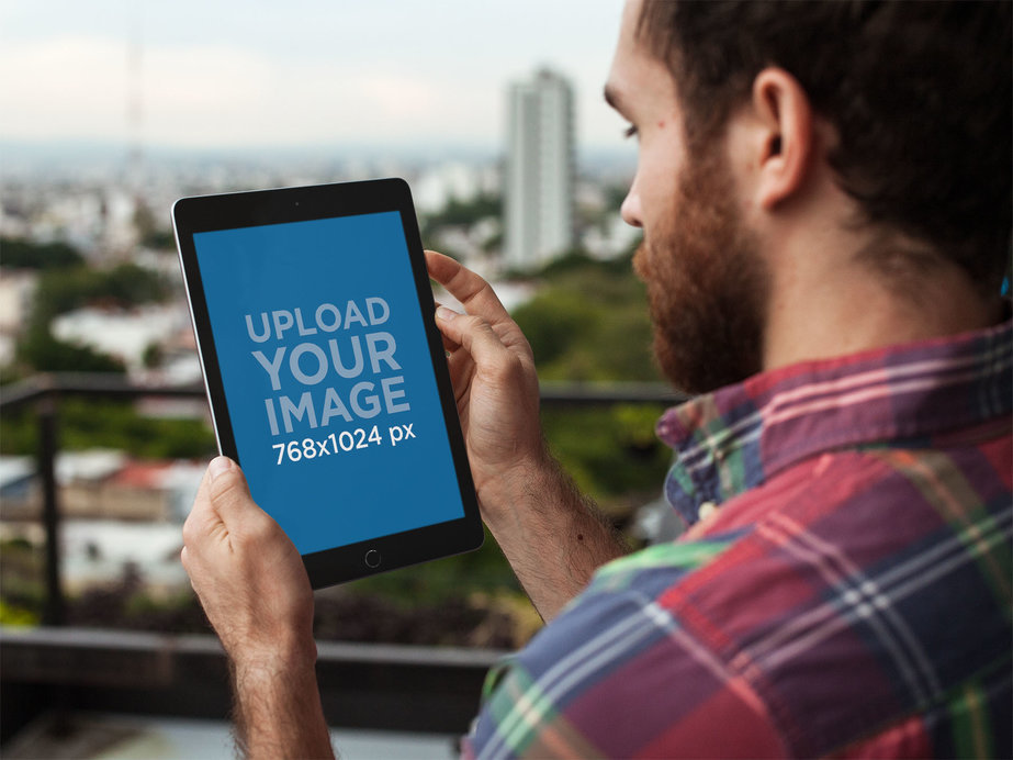 Mockup of a Man Holding a Space Gray iPad Facing the City