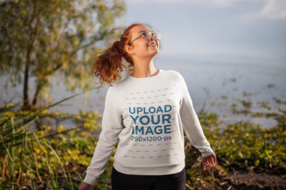 Mockup Featuring a Smiling Woman Wearing a Crewneck Sweater by a Lake