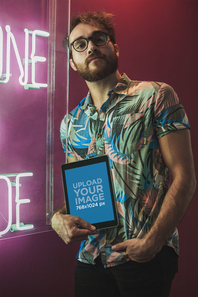 Mockup of a Man Holding a Space Gray iPad Leaning Against a Neon Sign 22609
