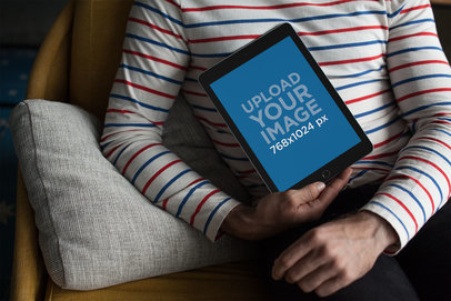 Mockup of a Man Holding an iPad Against his Torso Sitting on an Armchair 22613