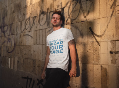 T-Shirt Mockup of a Man Leaning on a Graffiti Painted Wall
