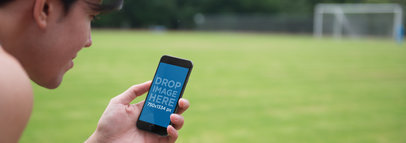 Mockup of a Young Man Using iPhone 6 at Soccer Field