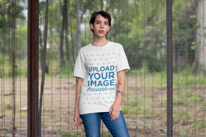 Mockup of a Woman Wearing a T-Shirt Standing in Front of a Tall Fence