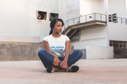 T-Shirt Mockup Featuring a Woman with Braids Sitting Outside a Warehouse