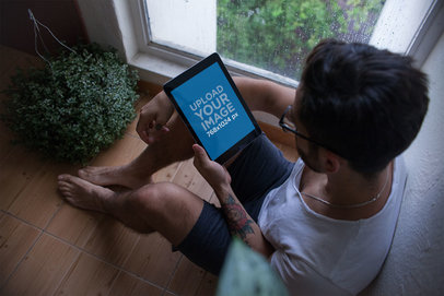 Mockup of an iPad Held by a Man Sitting Next to a Window on a Rainy Day 22827