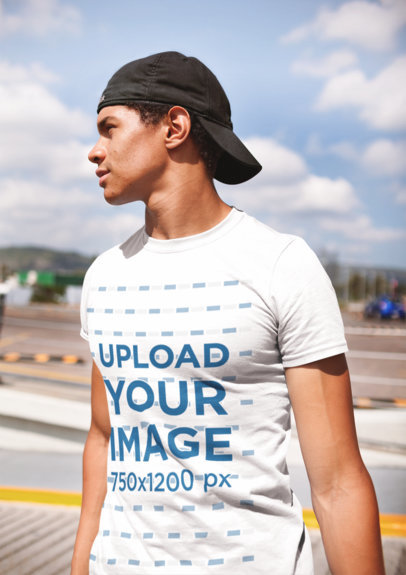 T-Shirt Mockup of a Man Standing in a Parking Lot on a Sunny Day