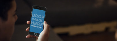 iPhone 6 Mockup of a Young Man Sitting on a Couch Using an iPhone
