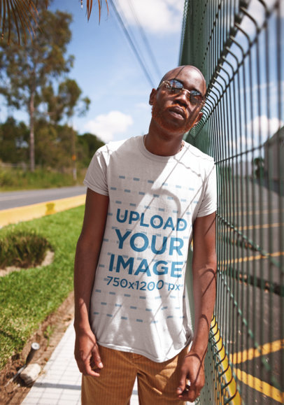 T-Shirt Mockup of a Man Leaning on a Metal Fence