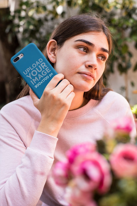 Mockup of a Woman Holding a Phone Case Near Flowers