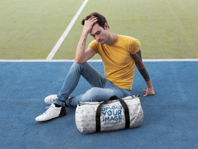 Mockup of a Man Sitting Next to a Duffle Bag at a Tennis Court