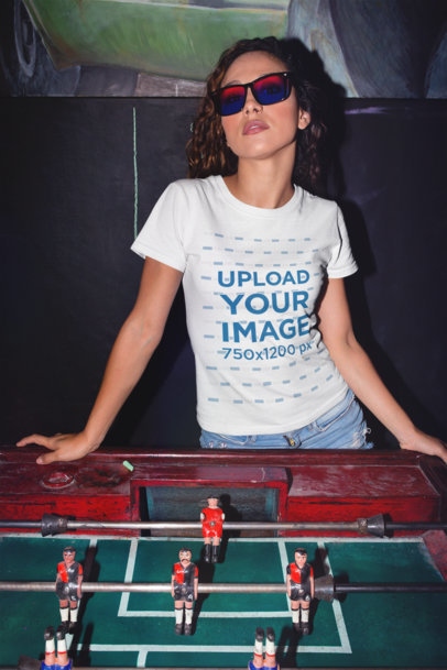 Mockup of a Woman Wearing a T-Shirt Leaning Over a Foosball Table