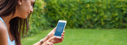 Mockup of a Young Woman Using an iPhone 6 at a Beautiful Garden