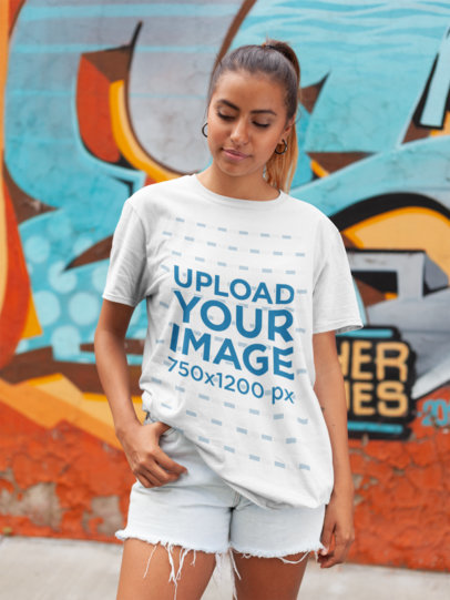 Mockup of a Woman Wearing a Unisex T-Shirt in Front of Graffiti