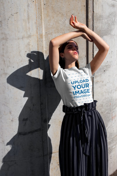 Tshirt Mockup of a Woman Blocking the Sun Leaning Against a Concrete Wall