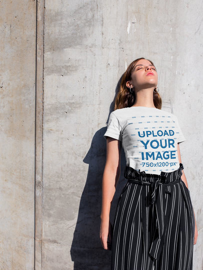 T-Shirt Mockup of a Woman Standing Against a Concrete Wall