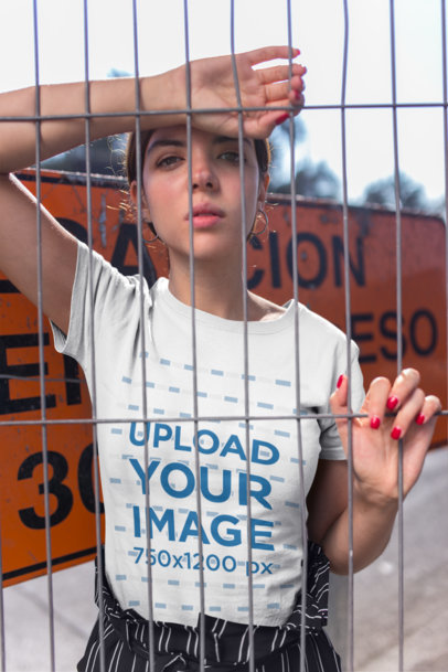 Mockup of a Trendy Woman Wearing a Tee Behind a Fence