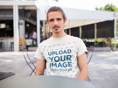T-Shirt Mockup of a Smiling Man Sitting at a Table Outside