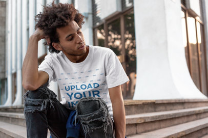Tee Mockup Featuring a Man with Afro Wearing Distressed Jeans in Front of a City Building
