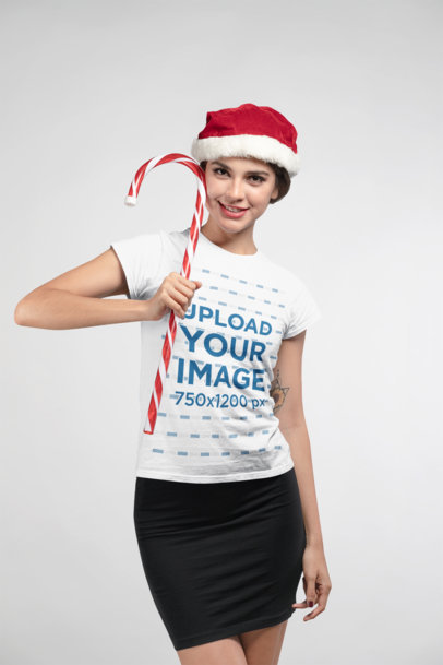 Christmas T-Shirt Mockup Featuring a Smiling Woman Wearing a Santa Hat and Holding a Candy Cane