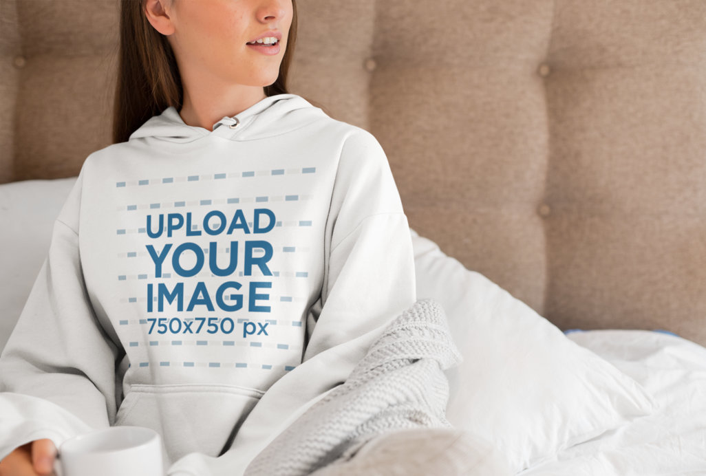 Pullover Hoodie Mockup of a Young Woman Sitting on a Bed with a Coffee Mug