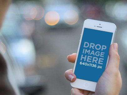 Mockup of a Woman Holding White iPhone 5 In the Street