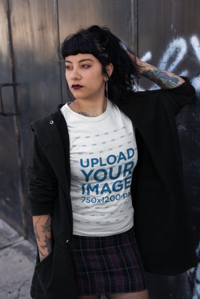 T-Shirt Mockup of a Thoughtful Goth Woman with Tattoos Leaning Against Wall 