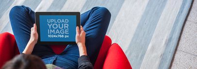 Tablet Mockup of a Young Woman Sitting on a Red Chair Using an iPad
