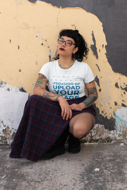 Tshirt Mockup of a Goth Woman Crouching Against a Rustic Old Wall