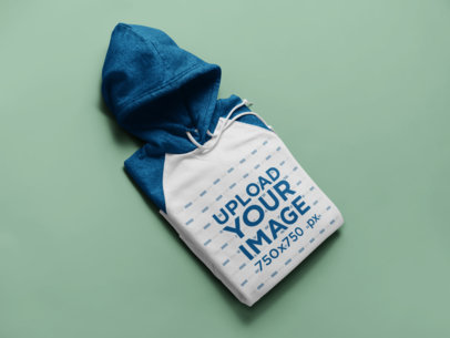 Mockup of a Raglan Hoodie Laid Over a Solid Colored Surface 24218