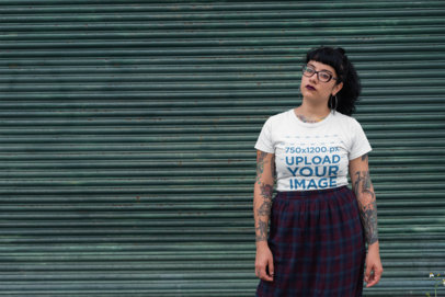 Tee Mockup of a Serious Woman with a Gothic Style Standing In Front of a Rusty Metal Curtain