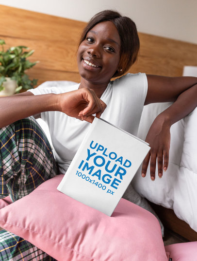 Mockup of a Smiling Woman Holding a Hard Cover Book Against a Pillow