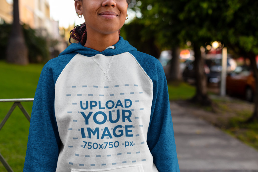 Mockup of a Woman Wearing a Raglan Hoodie on a Sidewalk