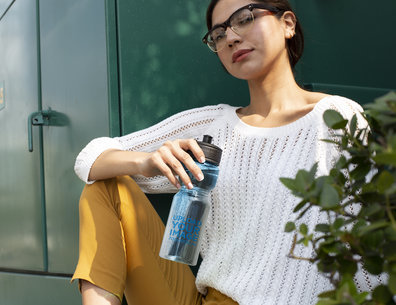 Water Bottle Mockup Featuring a Woman Sitting by a Green Electricity Container 24422