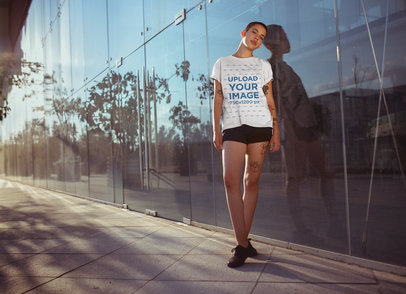 Tee Mockup of a Woman with Short Hair Leaning on a Building