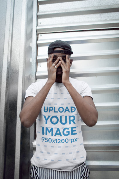 T-Shirt Mockup of a Man Hiding His Face Against a Metal Door