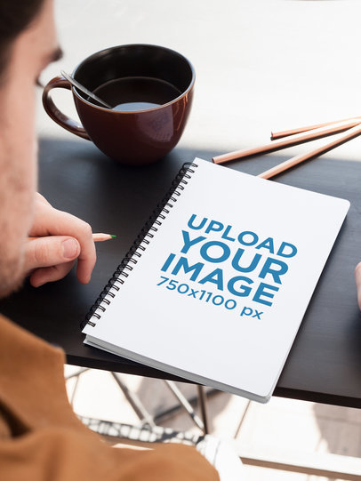 Mockup of a Notebook Placed on a Table Next to Colored Pencils