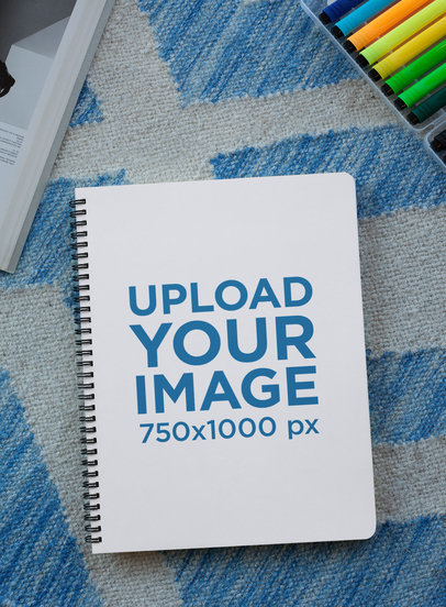 Mockup of a Notebook Lying over a Rug with Colorful Pens