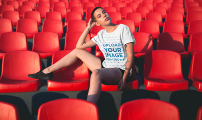 T-Shirt Mockup of a Short-Haired Girl Sitting in a Stadium with Red Seats 20182