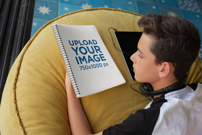 School Notebook Mockup Featuring a Young Boy at Home Looking at a Spiral Notebook Cover