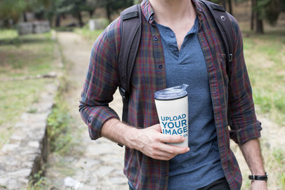 Mockup of a Man Holding a Travel Mug While Walking Outdoors