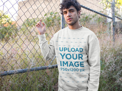 Heather Crewneck Sweater Mockup Featuring a Man Leaning Against a Fence 18182