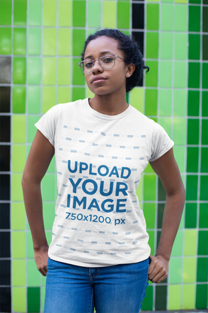 T-Shirt Mockup of a Woman with Glasses Standing in Front of a Green Mosaic