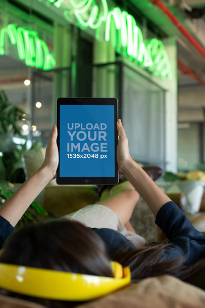 iPad Mockup Featuring a Woman Listening to a Podcast While Lying on a Sofa
