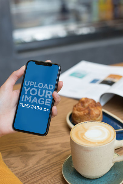 Mockup of a Woman Holding an iPhone 11 Pro While at a Cafe